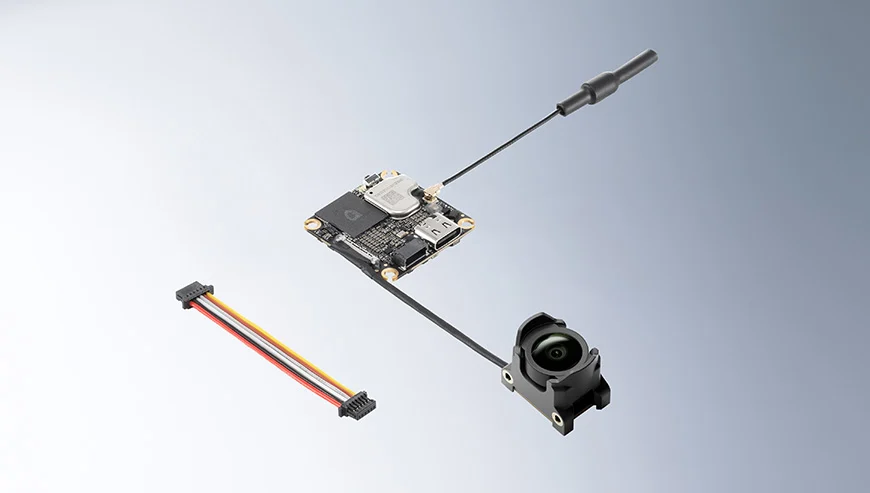 Moduł elektroniczny połączony przewodami z czarną anteną i obiektywem kamery, obok leży wielokolorowy kabel połączeniowy